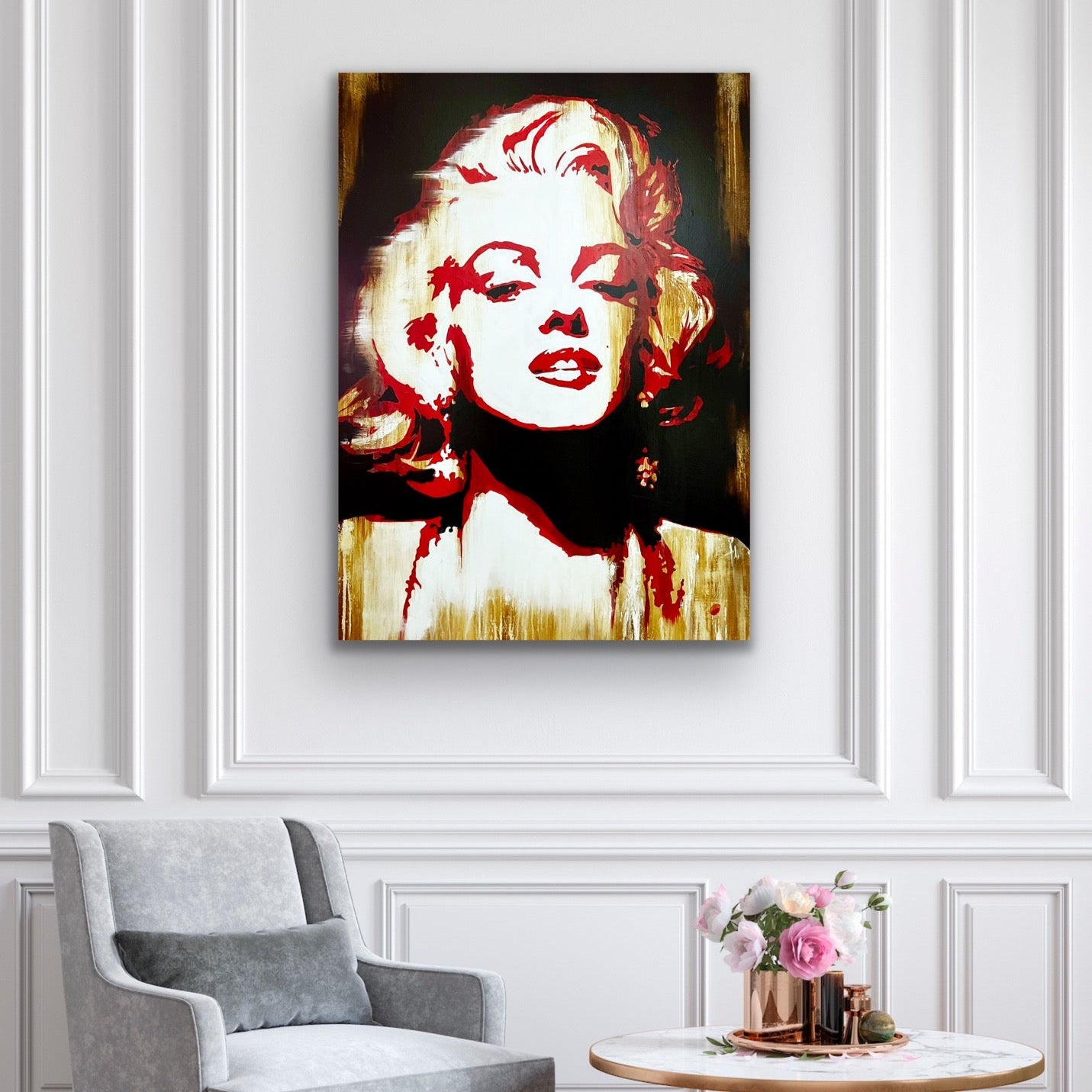 Framed artwork of a stylized portrait on a wall above a gray armchair.